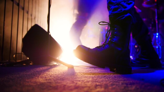 Rock concert guitarist in black massive boots playing guitar on stage feet close up