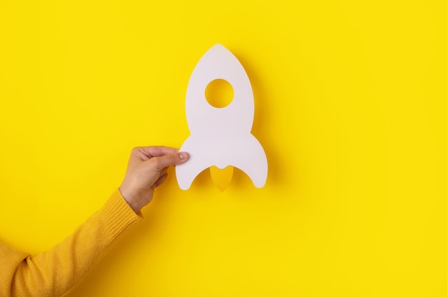 Rocket in hand over yellow background, startup business idea