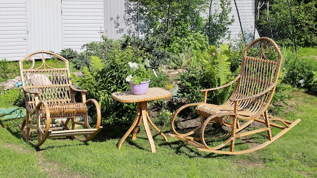 Rocking chair for recreation from rattan and small wicker table near flower bed