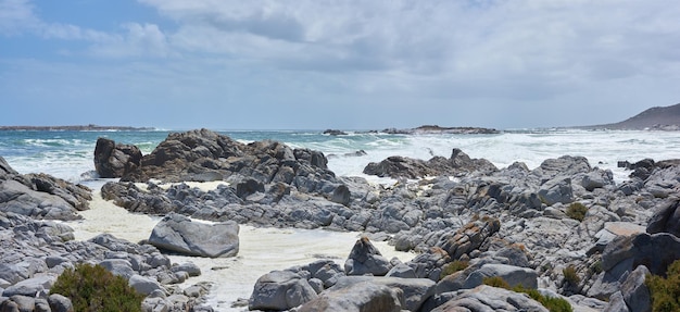 A rocky coastline at a beach in Cape Town with overcast clouds A shore with rocks at the ocean with some waves Rocky coast of mountain sea with on a cold day by a rock pool