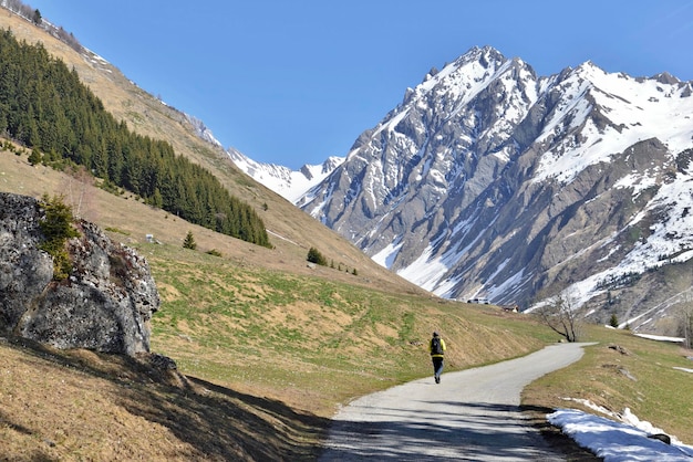 Rocky mountain still snowed in spring at the end of a road where walks the silhouette of a hiker in the franch Alps