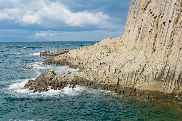 Rocky seashore formed by columnar basalt against the backdrop of a sea coastal landscape of the Kuril Islands