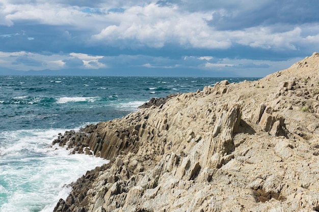 Rocky seashore formed by columnar basalt against the backdrop of a sea coastal landscape of the Kuril Islands