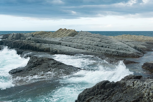 Rocky seashore formed by columnar basalt against the backdrop of a stormy sea coastal landscape of the Kuril Islands