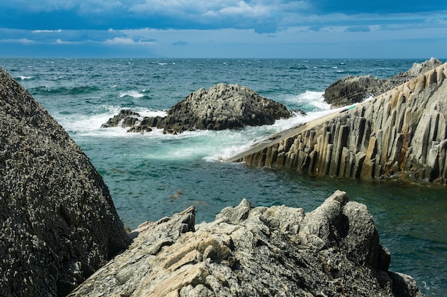 Rocky seashore formed by columnar basalt against the surf coastal landscape of Kunashir Island