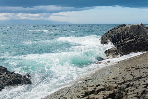 Rocky seashore formed by columnar basalt against the surf coastal landscape of the Kuril Islands