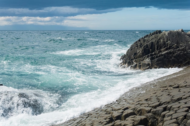 Rocky seashore formed by columnar basalt against the surf coastal landscape of the Kuril Islands