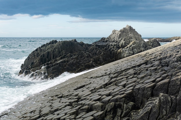 Rocky seashore formed by columnar basalt against the surf coastal landscape of the Kuril Islands