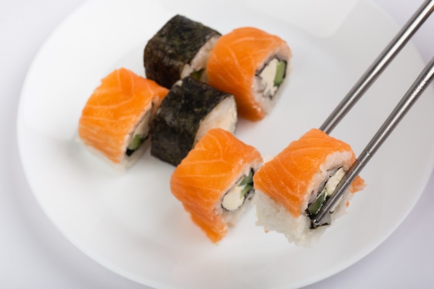 Roll of sushi on chopsticks with sushi roll on white plate on white background