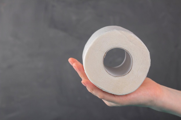 A roll of toilet paper lies on a woman's palm on a gray background