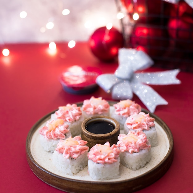 Roll with cream cheese on red with garland lights. Sushi rolls topped with pink cream and shrimp