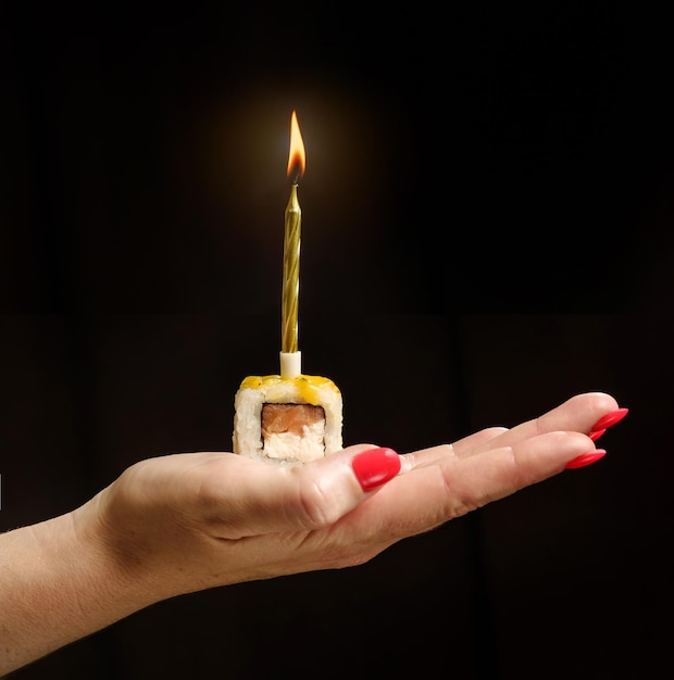 Roll with a festive candle on a female palm on a black background