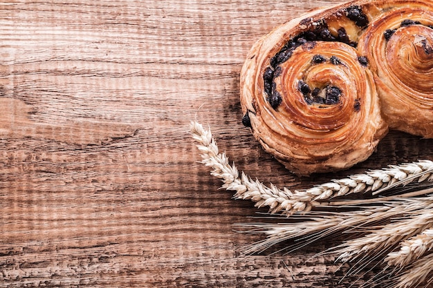 Roll with raisins wheat ears on oak wooden board food and drink concept