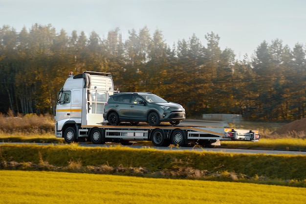 Photo a rollback tow truck transports a broken car on the public road car failure during the journey roadside assistance in action