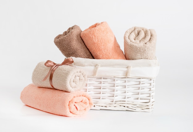 Rolled different colors terry towels with a ribbon against a white backdrop, towels in a white basket in front of a white backdrop