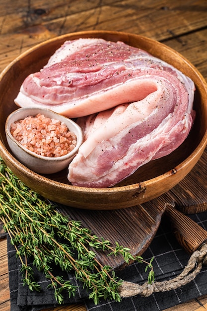 Rolled Pork belly raw meat in a wooden plate with thyme Wooden background Top view