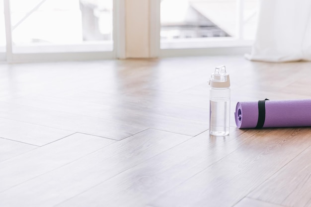 Rolled purple yoga mat and clear plastic water bottle on a wooden surface with natural light Genderneutral fitness yoga and exercise props at home or gym banner with copy space Active lifestyle