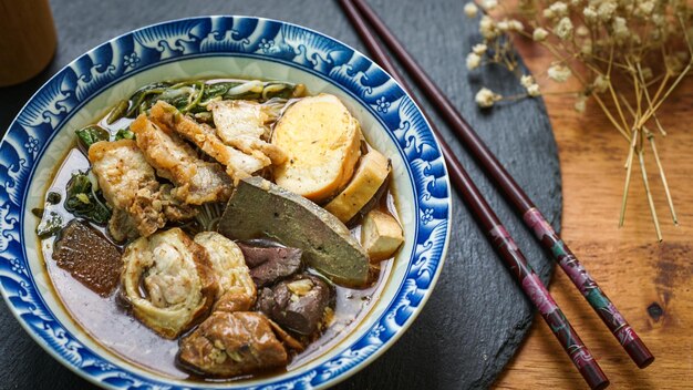 Rolled Rice Noodles in Fivespices Broth served in a tiled cup on a wooden table