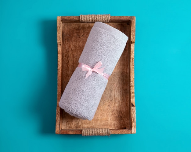 Rolled terry towel tie up by pink ribbon on the rustic style wooden tray