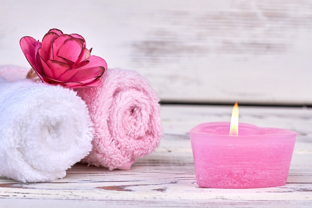 Rolled towels with burning candle on white background