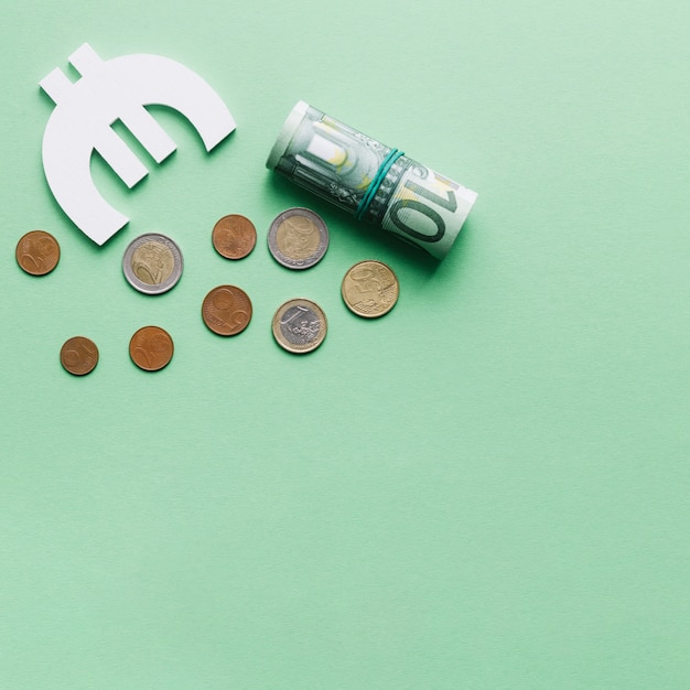 Rolled up hundred euro note with symbol and coins on green backdrop