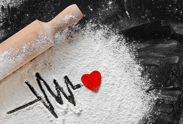 Rolling pin on blackboard with Heartbeat shape made with flour and red heart