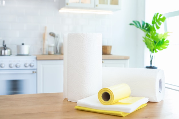 Rolls of paper towels, cleaning wipes and garbage bags on the table in the kitchen with sunlight.