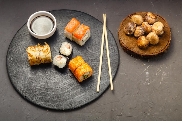 Rolls with fish and shrimp on a round board next to sticks soy sauce and baked champignons