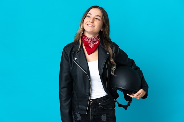 Romanian woman holding a motorcycle helmet isolated on blue wall thinking an idea while looking up