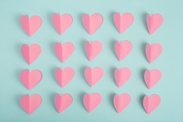 Romantic background made of pink paper hearts on blue background. Paper cut pink hearts