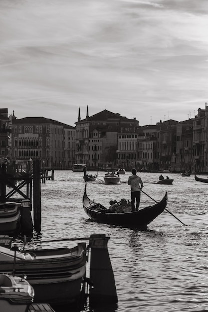 Romantic black and white photo of tourists sitting in a gondola with a gondolier floating down a