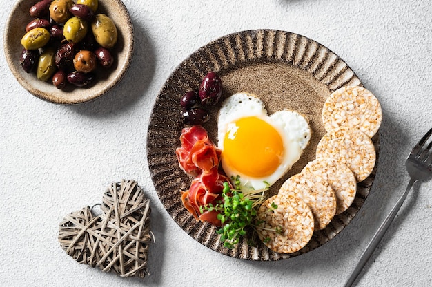 Romantic Breakfast on Women's Day - fried eggs in the shape of a heart and olives. Healthy breakfast. Rice cakes with eggs and hamon. Romantic breakfast. Top view.