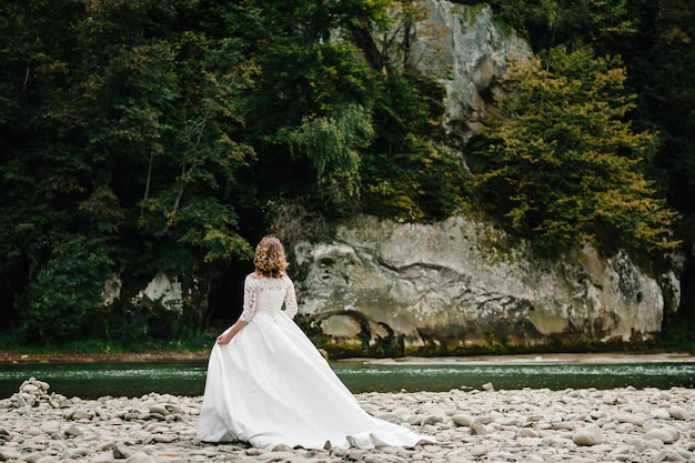 Romantic bride standing on the stony shore river in the mountains The bride walking on nature Back view Country