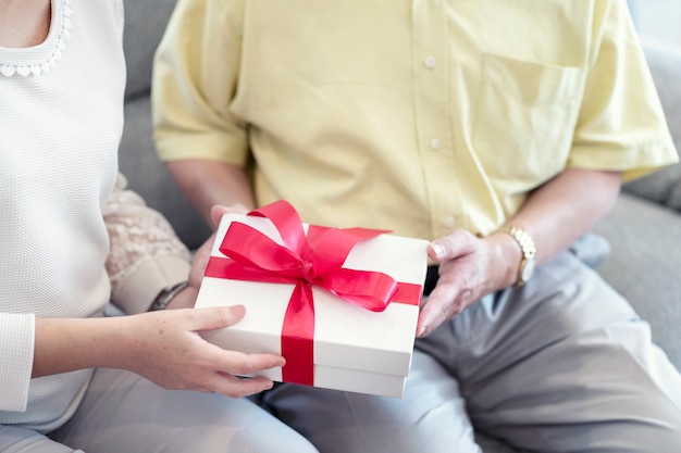 Romantic couple, Husband holding surprise gift box for her wife sitting on couch together.