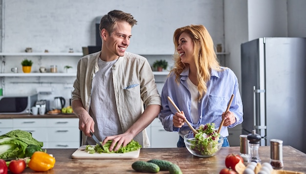 Romantic couple is cooking on kitchen. Handsome man and attractive young woman are having fun together while making salad. Healthy lifestyle concept.