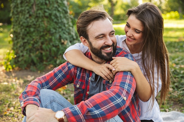 romantic couple man and woman dressed in casual wear hugging while resting in green park