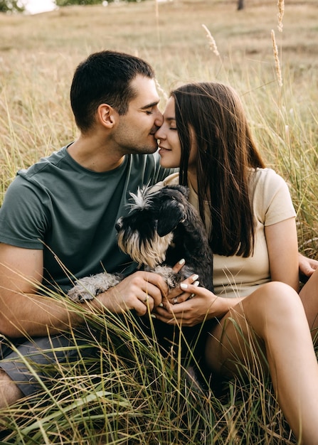 Romantic couple of man and woman sitting outdoors hugging a miniature schnauzer purebred dog smiling