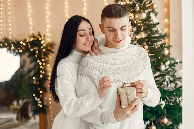 Romantic couple standing near Christmas tree and holding a gift box