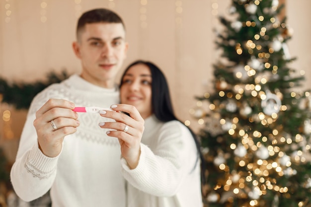 Romantic couple standing near Christmas tree and holding a positive pregnancy test