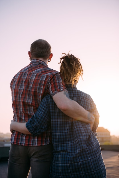 Romantic date outdoors. Cuddling love couple. Unrecognizable people together enjoying sunset on roof, stylish modern hipsters in focus on foreground, urban background with free space