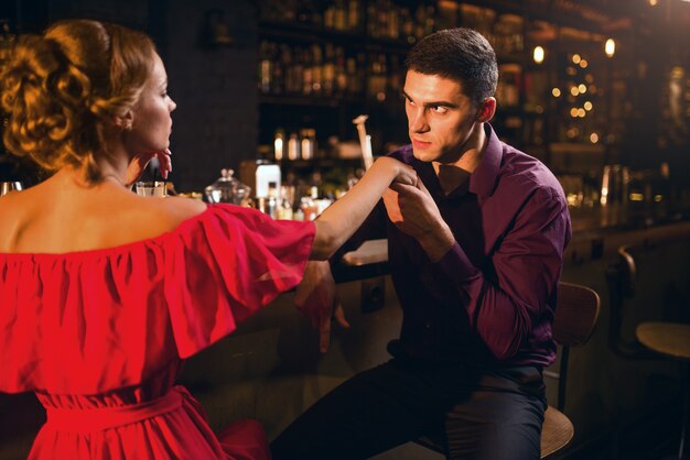 Romantic date in restaurant, attractive woman in red dress flirts with man against bar counter. Love relationship, night lifestyle