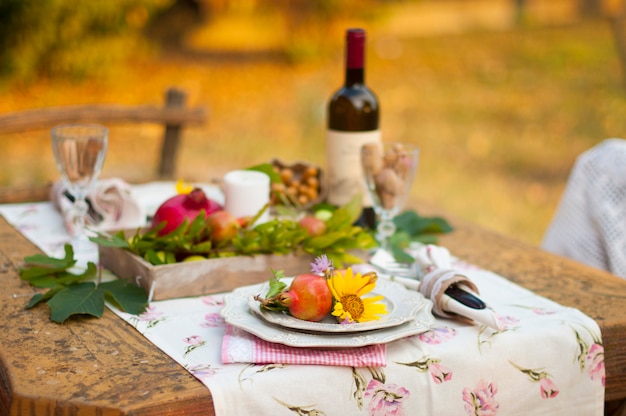 Romantic dinner in the autumn garden, table setting for a nice dinner. Wine, fruit, pomegranate and flowers. Picnic in the open air.