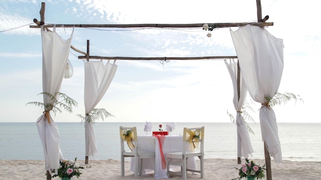 Romantic dinner table set and chair preparation with white theme decoration white sand clear cloudy sky and tranquil peaceful beautiful beach view at the seashore Good place for wedding proposal