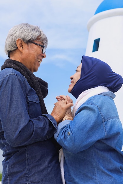 Romantic elderly couple facing each other and holding hands with blue sky background