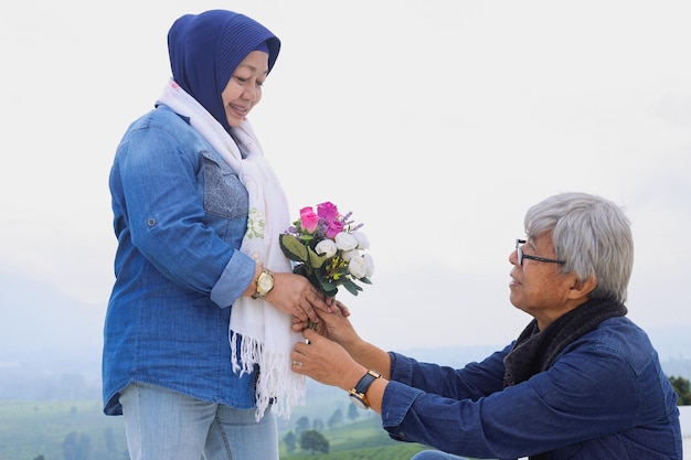 Romantic elderly couple Husband is bend a knee and giving flower to wife Wedding anniversary