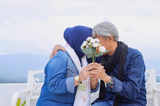 Romantic elderly couple kissing and covering their face together with white flower