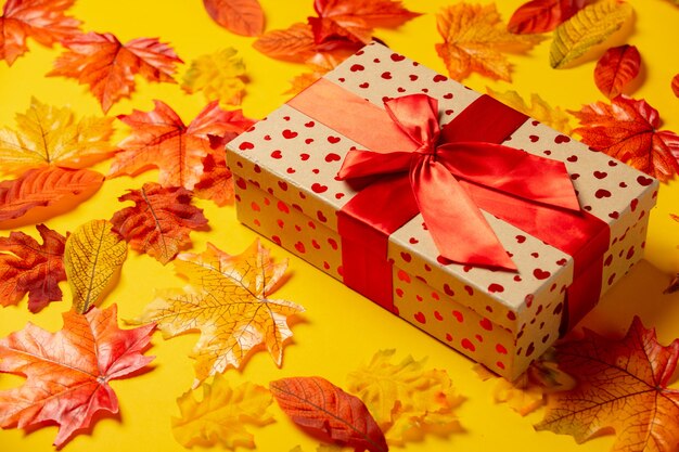 Romantic gift box with autumn leaves on yellow background. Top view