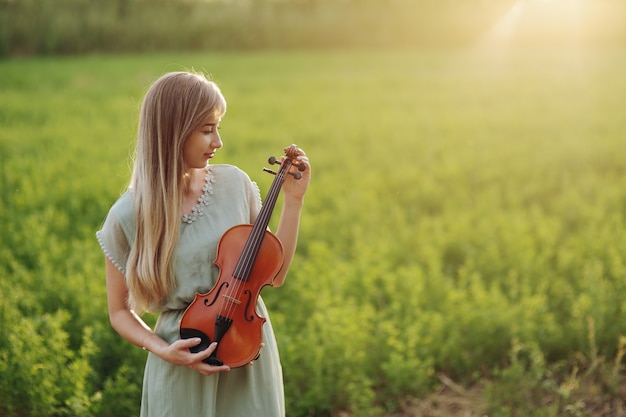 Romantic girl with loose hair holding a violin in her hands in the sunset light