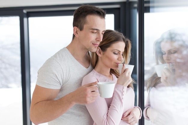 romantic happy young couple enjoying morning coffee by the window on cold winter day at home