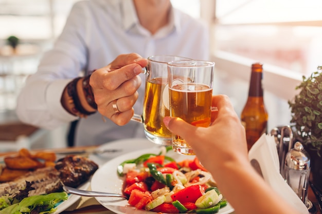 Romantic honeymoon dinner for two. Couple toasts and drinks alcohol. People eat greek salad and seafood in cafe